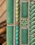Detail shot of custom-cut rope motif tiles in Aurora Iridescent and Pewabic Green glazes. There is also a traditional Pewabic accent tile featured at the photo's center.