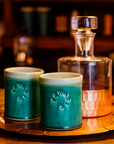 The Rocks Cups are short, cylindrical cups with smooth, straight sides. The Pewabic logo is stamped onto the side. There are two glazes featured on each cup - one is on the outside, covering the logo while the other glaze is on the inside of the cup and spills over creating a half inch ring around the outer lip of the cup.