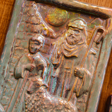 The Shepherds Tile features a man dressed in robes with his hand on the shoulder of a young boy. A sheep stands at their feet and the moon looks down at them through a large hole in the brick wall behind them.