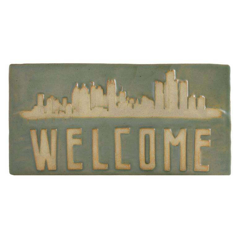 This Detroit Welcome Tile features the Detroit skyline above the word "Welcome" written in a bold font. The background is a satin green glaze while the word and skyline have been scraped giving them a creamy beige color.