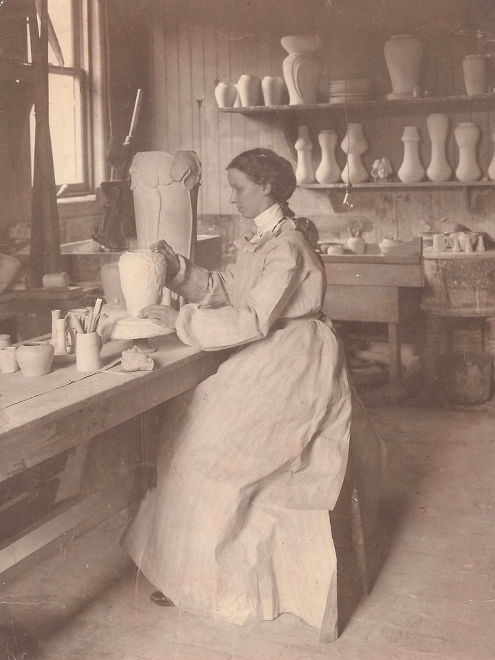 Mary Chase Perry Stratton sculpting with a historic lotus vessel set beside her in the Stable Studio circa 1904.