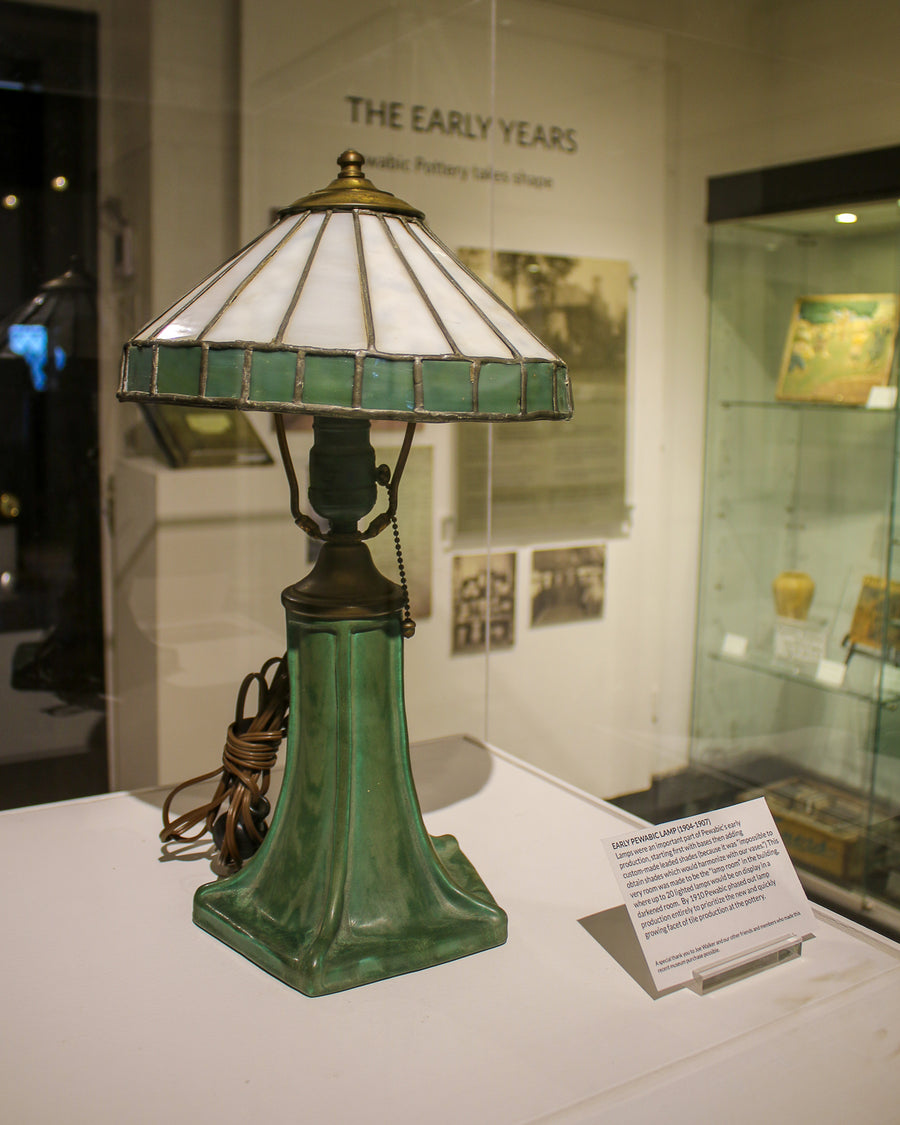 Photo of a matte green glazed lamp from Pewabic's museum collection on display in the exhibition entitled "Pewabic: Detroit's Pottery"