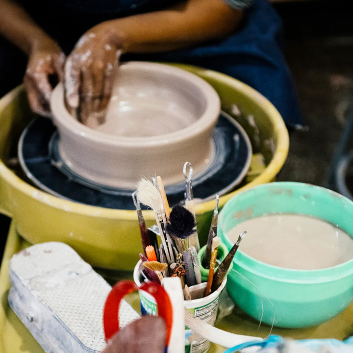 Close-up photo of a Pewabic student's hands as they wheel-throw a custom piece.  