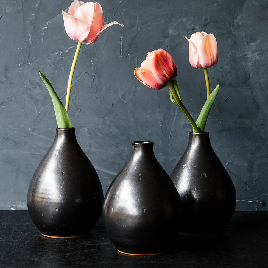 Three Teardrop Vases in our Greenstone glaze with dark, iron speckles on a wooden dining table with fall foliage.