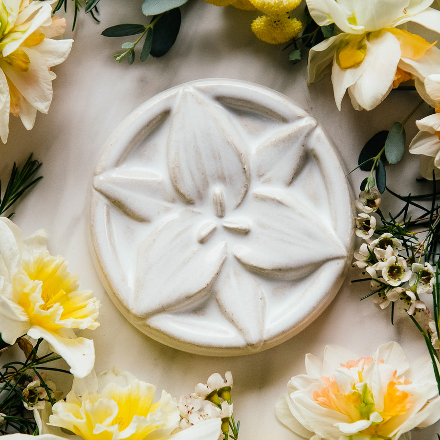 This circular tile has a high relief trillium flower centered within the design. It petals stretch out to the very edges of the circle and overlap the tile's simple line border.