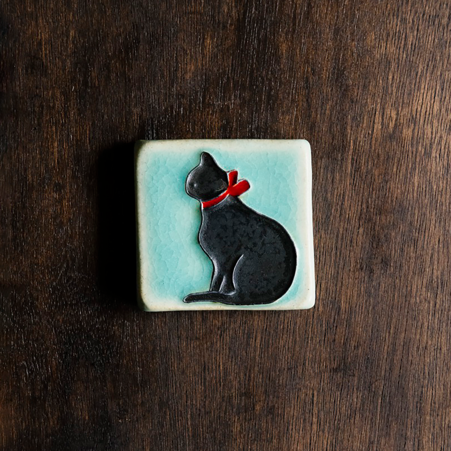 This Cat Tile features a black cat wearing a bright red bow around its neck on a pale blue background.