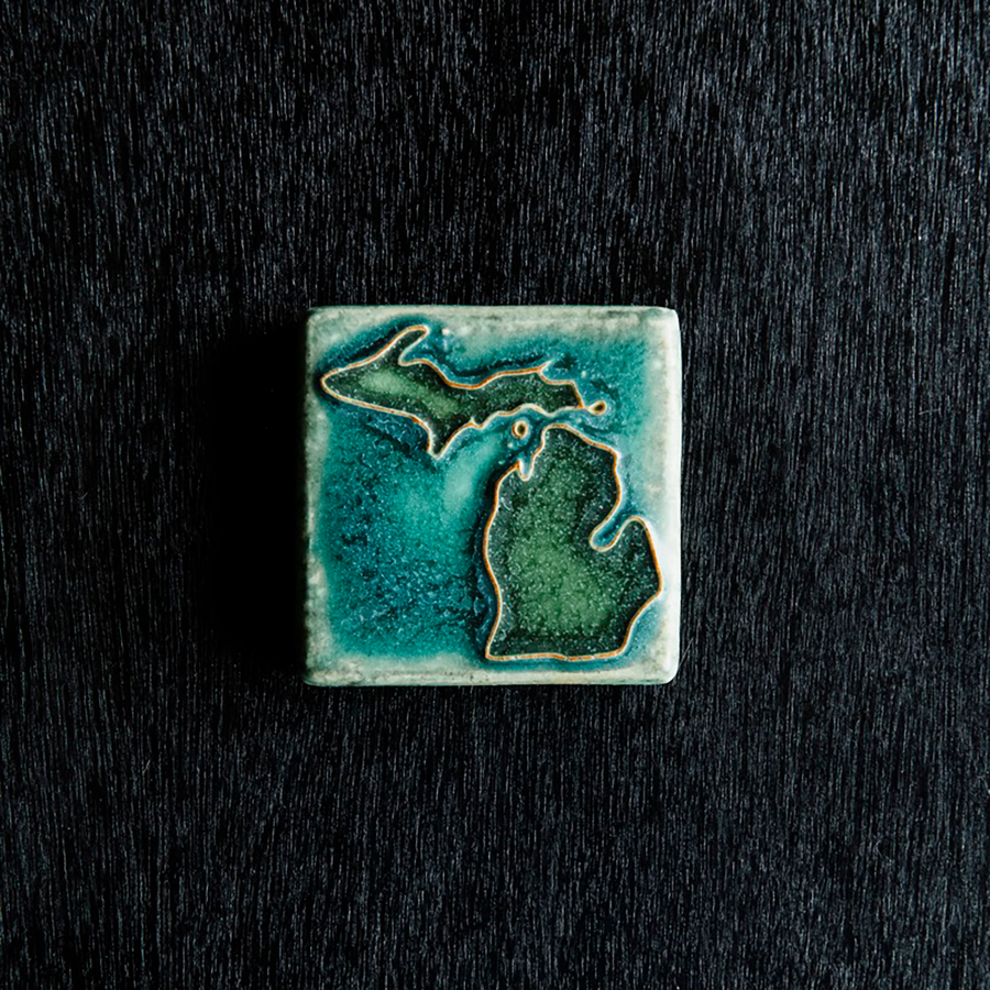 This hand painted tile has a matte turquoise background with matte earthy green peninsulas.