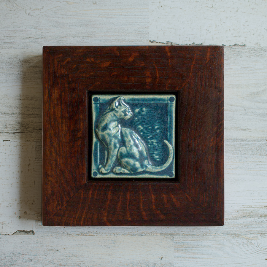 The 3D Cat Tile features a sleek cat sitting up straight with its head turned backward towards its flicking tail. The tile is in the matte french blue Peacock glaze which beautifully offsets the deep reddish brown of the oak wood frame.