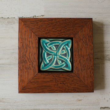 The Lover's Knot Tile features a central ring with four corner loops weaving around the ring from the corners to the center of the tile. This tile is in our matte turquoise Pewabic Blue glaze which beautifully offsets the deep reddish brown oak wood frame.