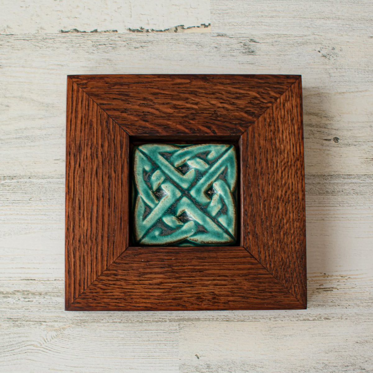 The 3 inch square Eternity Knot Tile includes the design of two oval shapes intertwined to create the Celtic Eternity knot. This tile features the matte turquoise Pewabic Blue glaze which beautifully offsets the deep reddish brown oak wood frame.