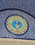 A detailed photo of the iconic peacock lunette fixed above the doorway to the Bird House at the Detroit Zoo. The peacock is set within a circular shape, with distinctive and delicate flower motif tiles bordering the design. This photo also includes details of the blue and iridescent tiles encompassing the intricate peacock feature.