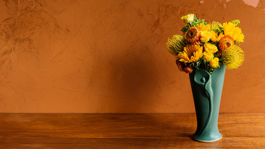 Elm Calla Vase with flowers on a wooden surface against an orange wall