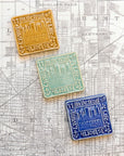Three decorative Old Detroit tiles in glossy Honey, Celadon, and Lake Superior glazes on a map of Detroit background.  