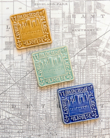 Three decorative Old Detroit tiles in glossy Honey, Celadon, and Lake Superior glazes on a map of Detroit background.  