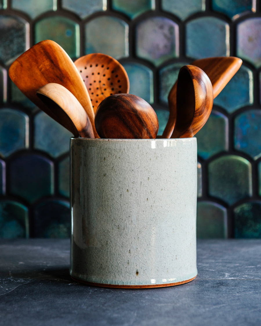 A textured ice-blue Frost glaze holding teakwood utensils with an Aurora Iridescent tile wall. 