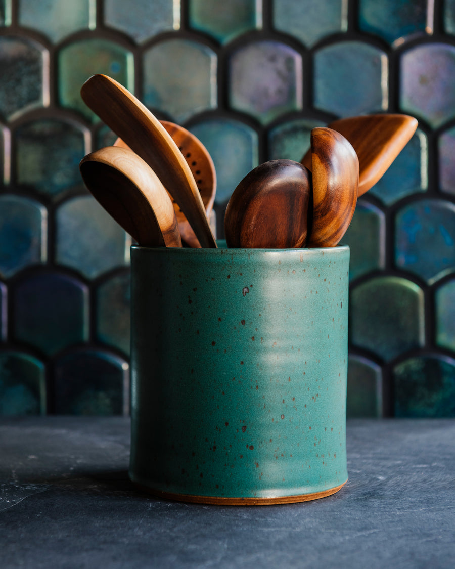 Floral arrangement in a freckled Greenstone vase with teakwood utensils against an Aurora Iridescent tile wall. 