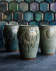 Three glossy, deep green Balsam Pinecone vases against an Aurora Iridescent tile wall. 