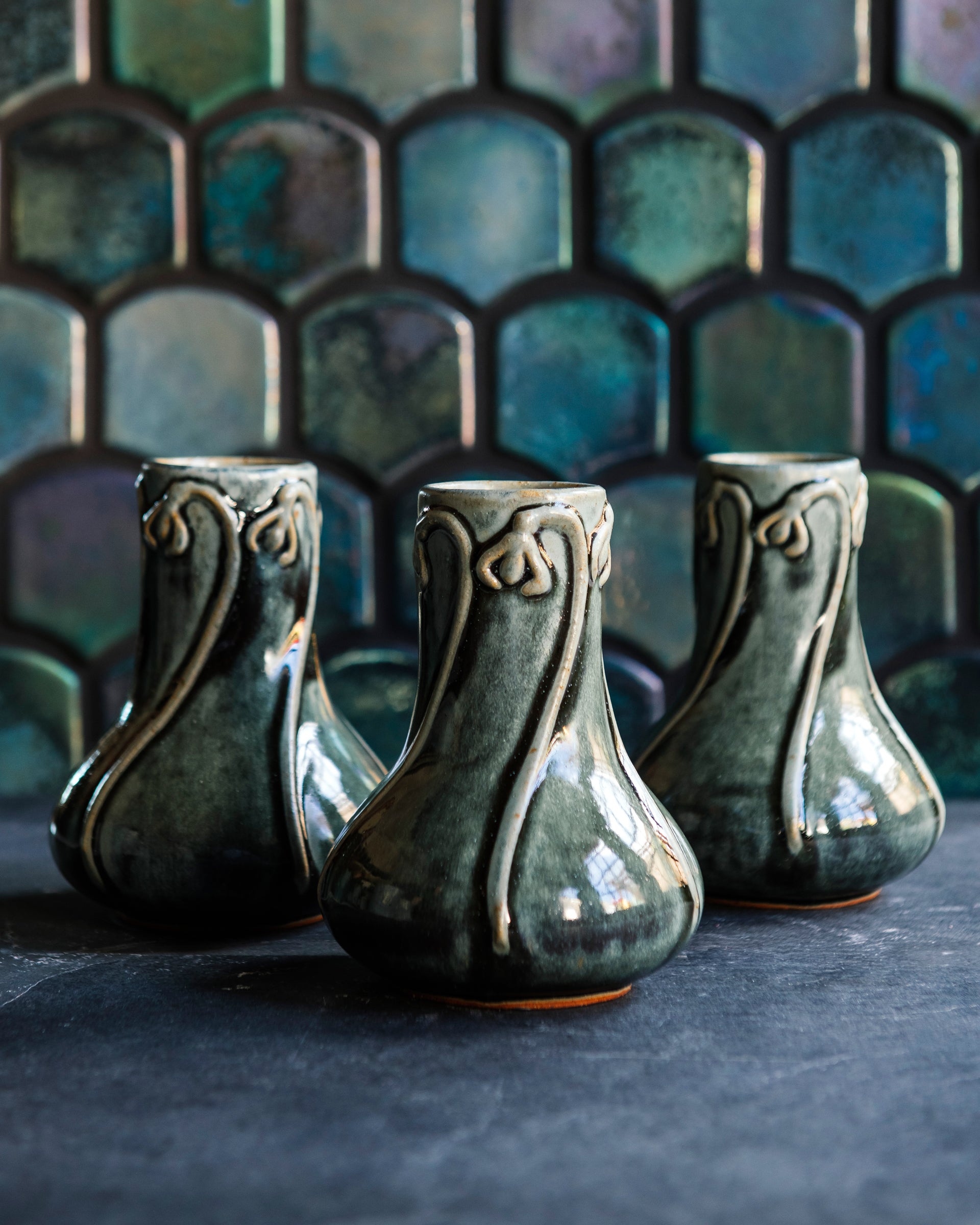 Three glossy, deep green Balsam Snowdrop vases against an Aurora Iridescent tile wall. 
