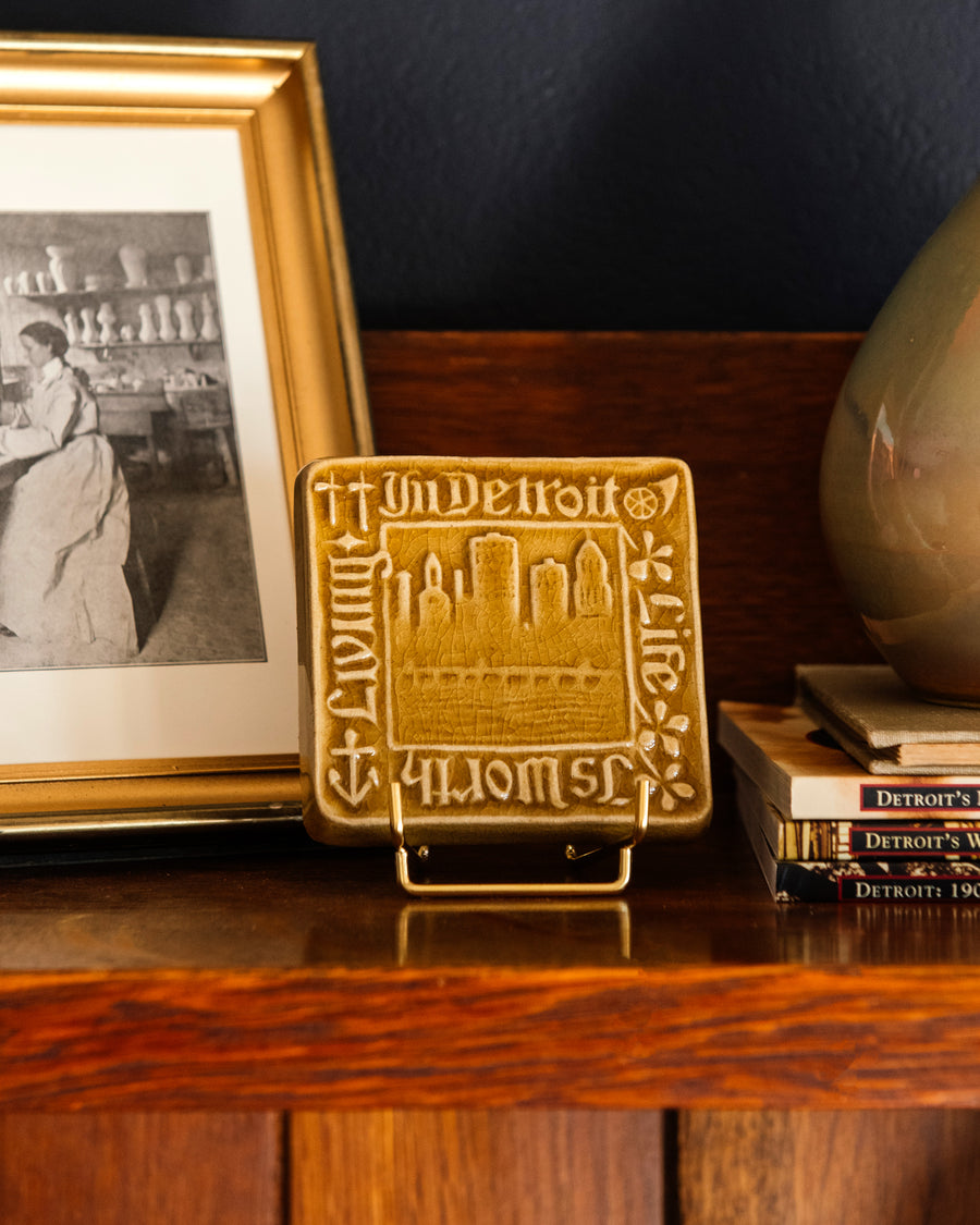 Decorative Old Detroit tiles in glossy Honey glaze on a handcrafted Stickley cabinet  next to a stack of books and framed photo. 