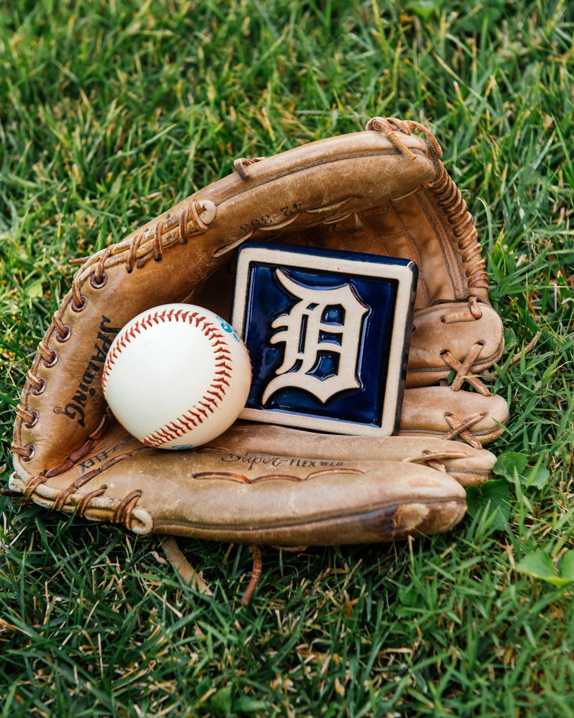 Baseball glove with a baseball and a Detroit Tigers tile in the grass. 