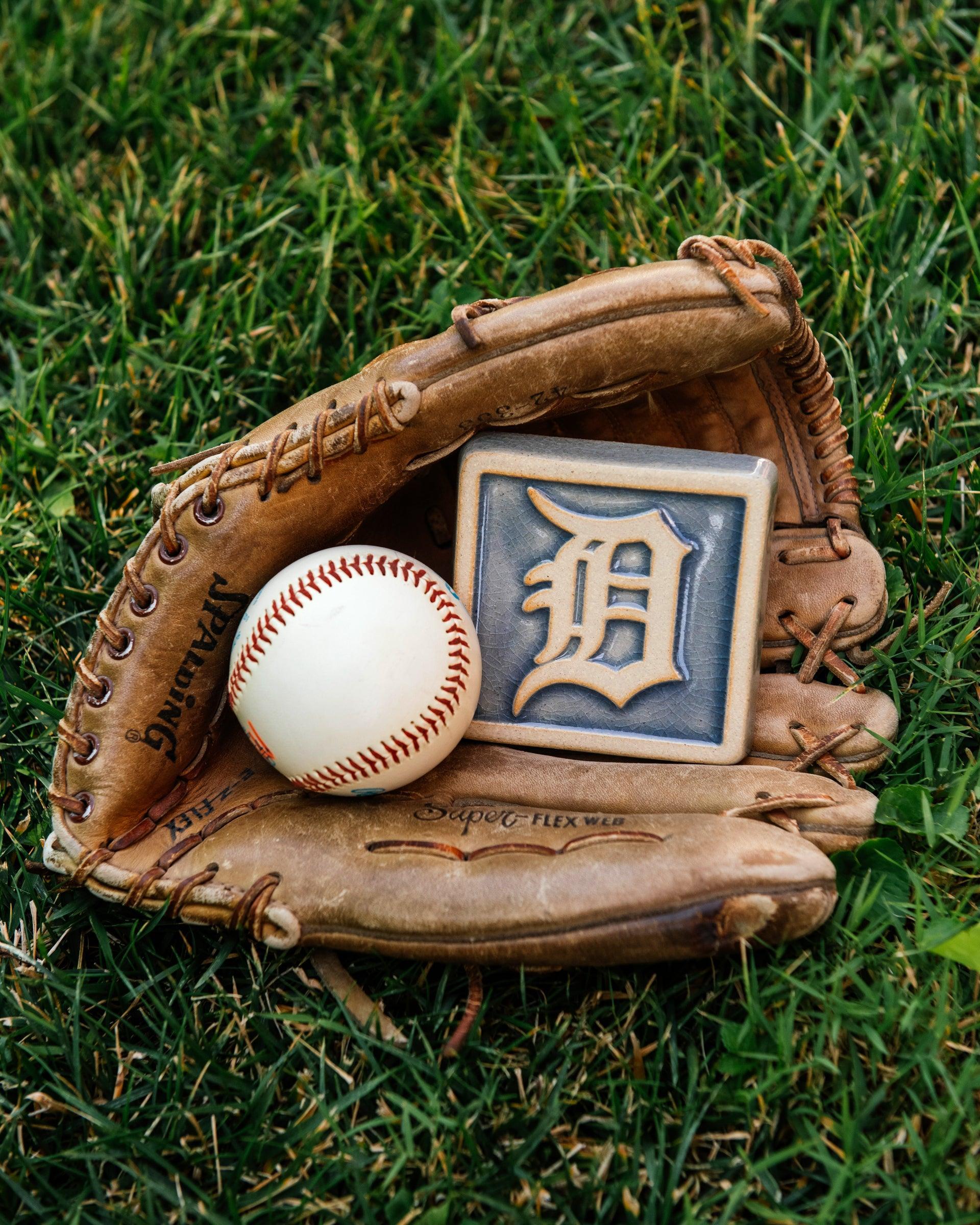 Baseball glove with a baseball and a Detroit Tigers tile in the grass. 