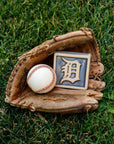 Baseball glove with a baseball and a Detroit Tigers tile in the grass. 