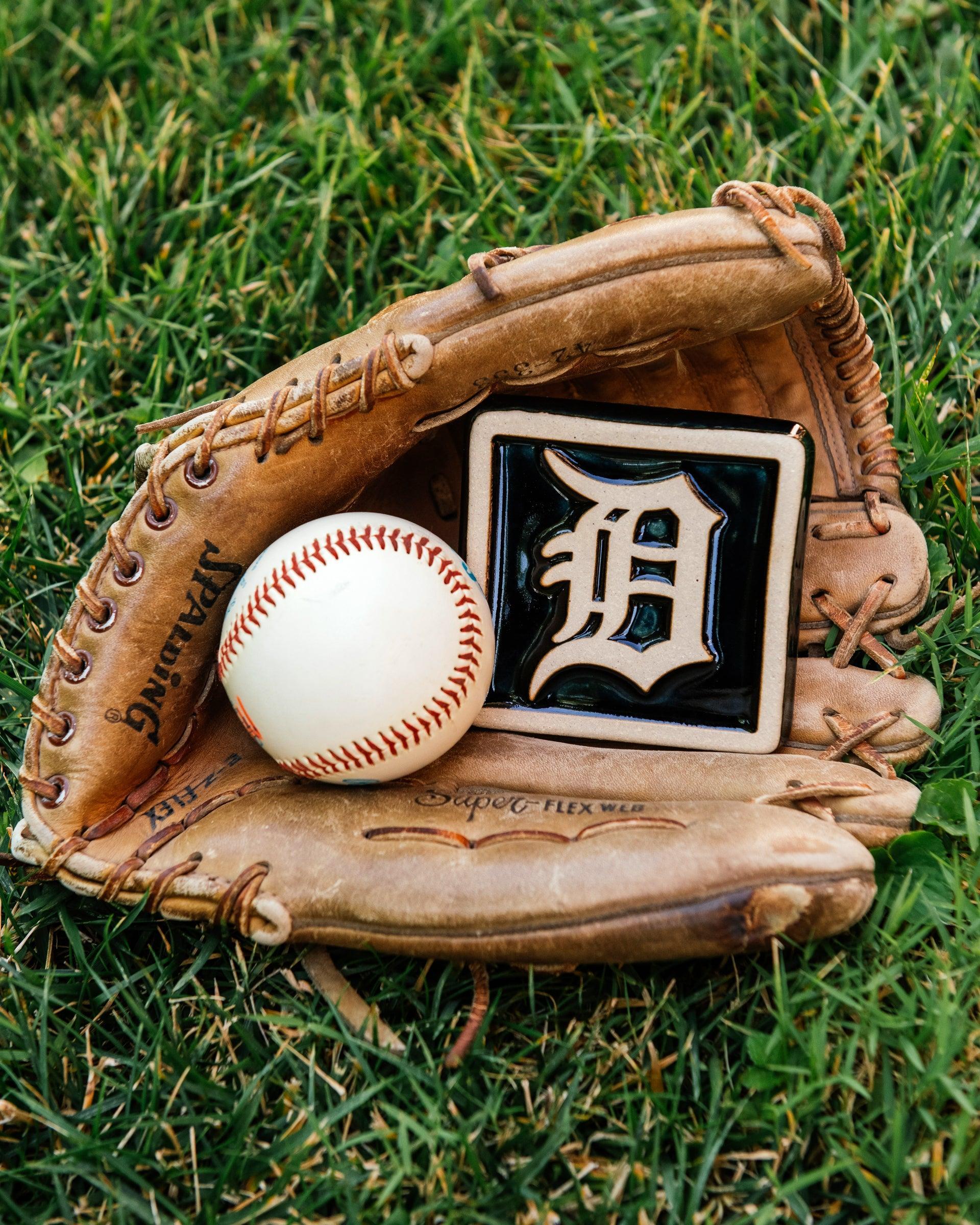 Baseball glove with a baseball and a Detroit Tigers tile in the grass. 