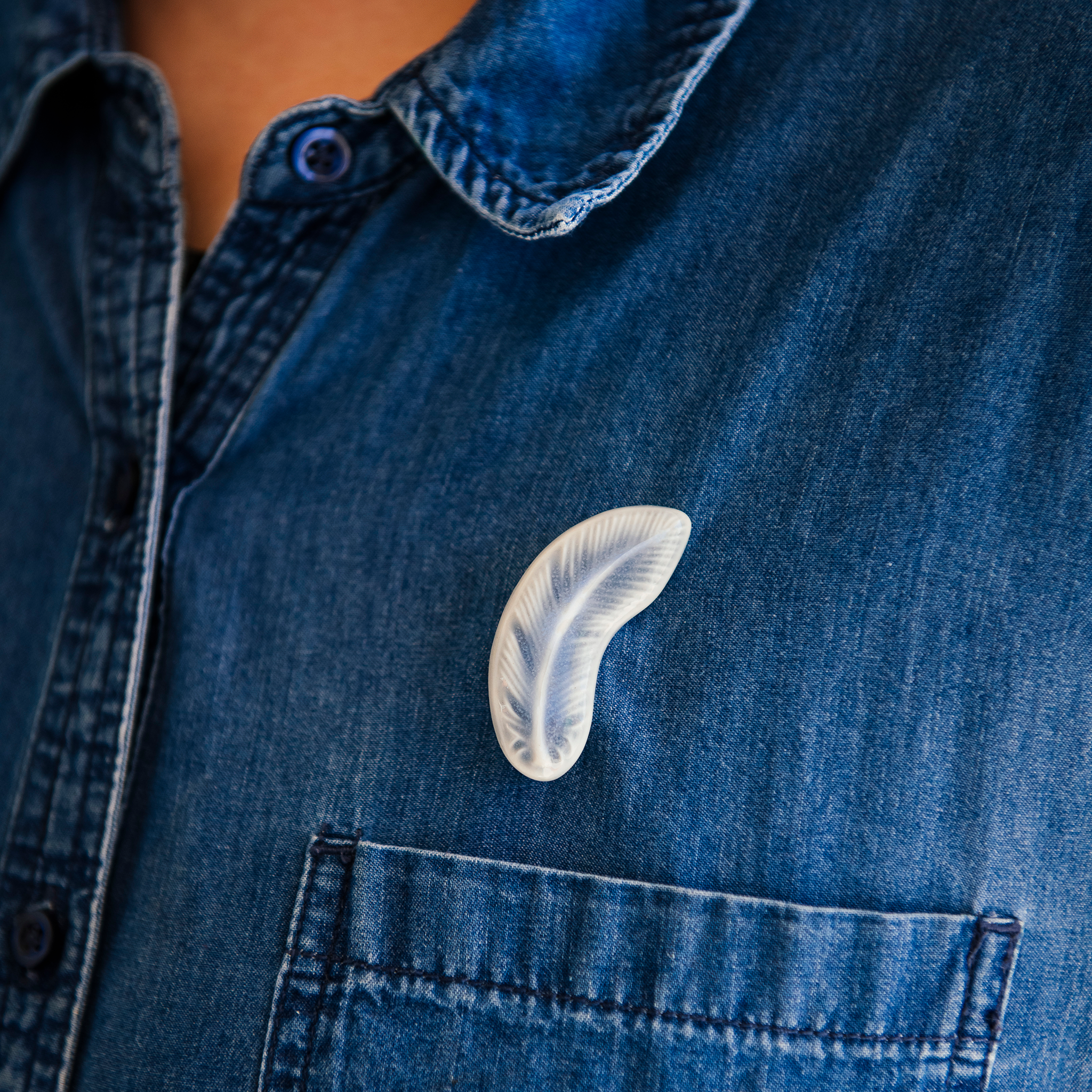 The pale color of the Feather pin is stark against a bright jean button down shirt.