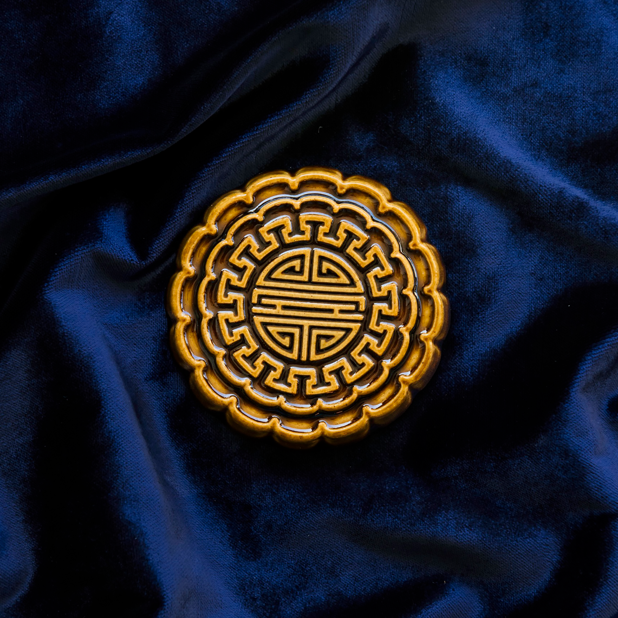 A Mooncake Paperweight in our glossy Molasses glaze on a rich, blue velvet.