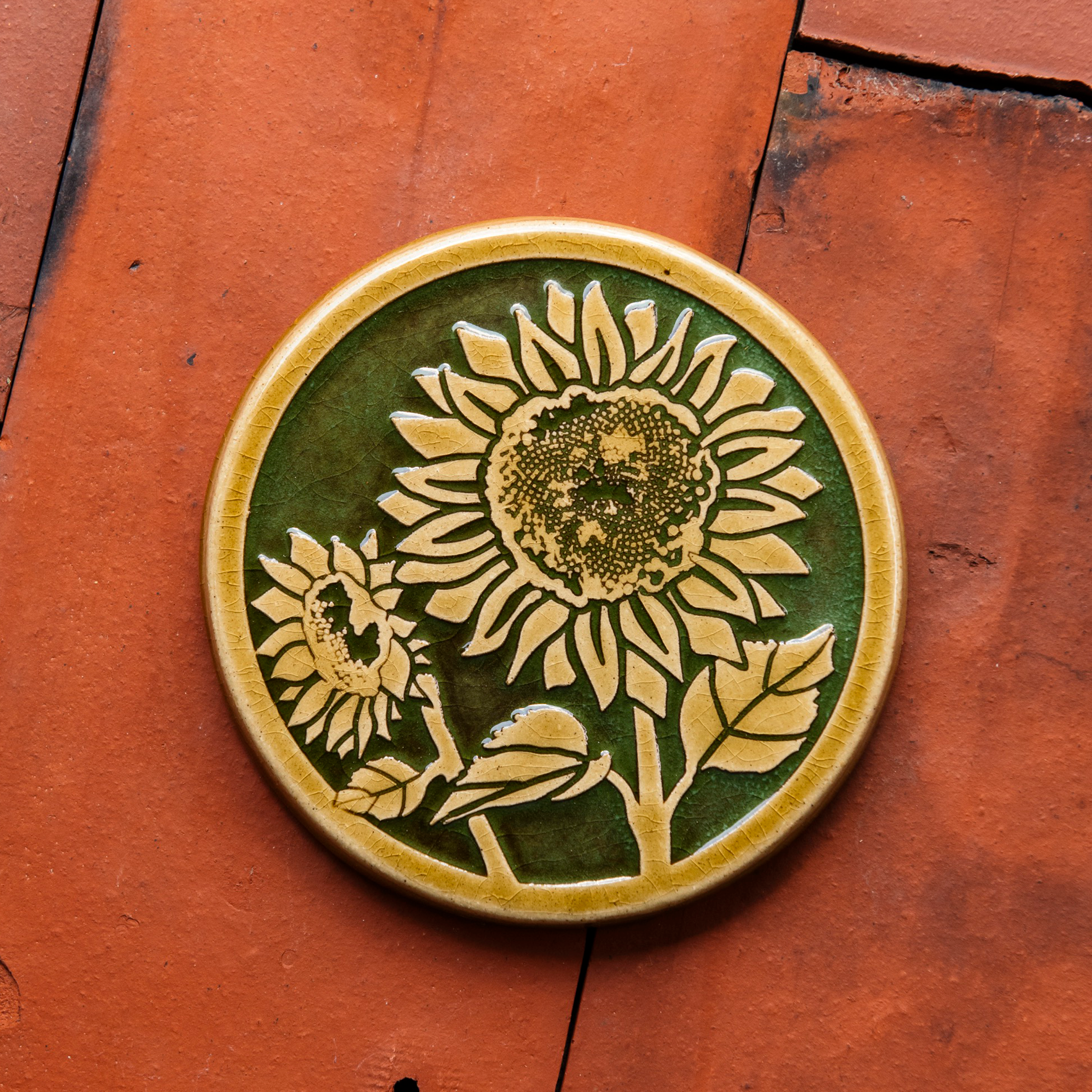 A two-tone glossy, round Sunflower Trivet with golden border and outline set against an emerald green background. 