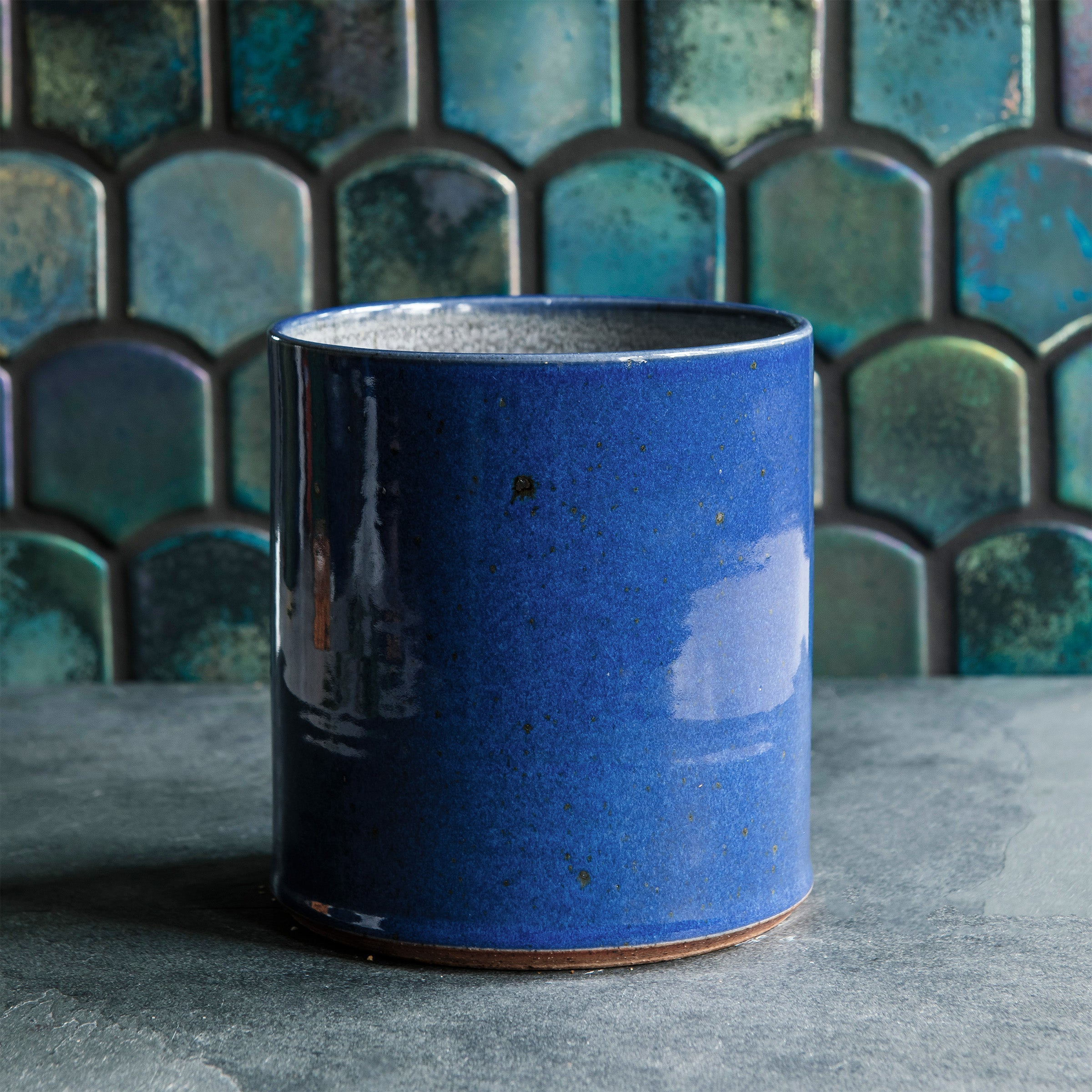 A close-up of the Crock in Ultramarine shows a smooth, glossy blue surface. Small brownish grey iron spots dapple the surface of the vase.
