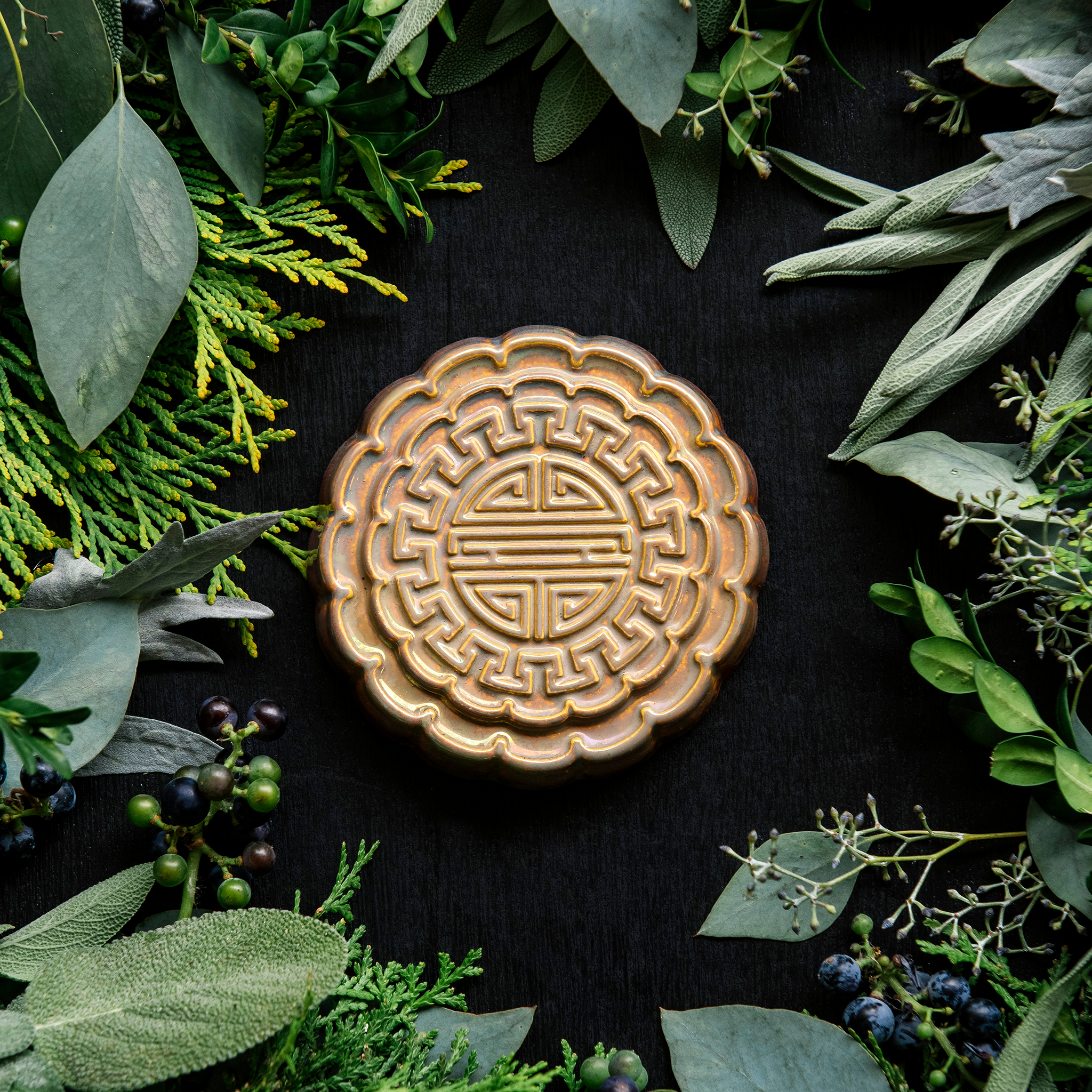 A Mooncake Paperweight in shimmering Blush Iridescent surrounded by cool greenery and delicate concord grapes. 