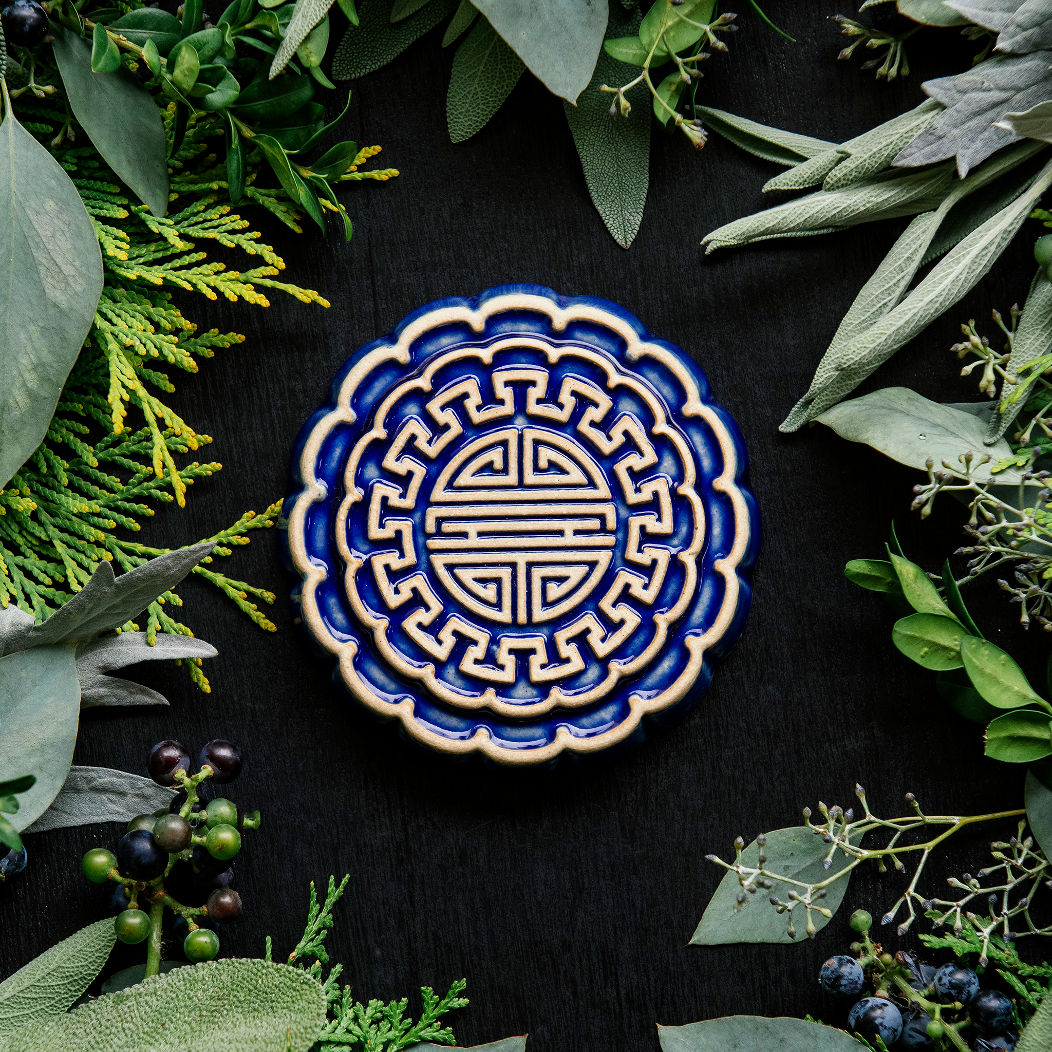 A Mooncake Paperweight in two-tone Lapis/Scrape surrounded cool greenery and delicate concord grapes.