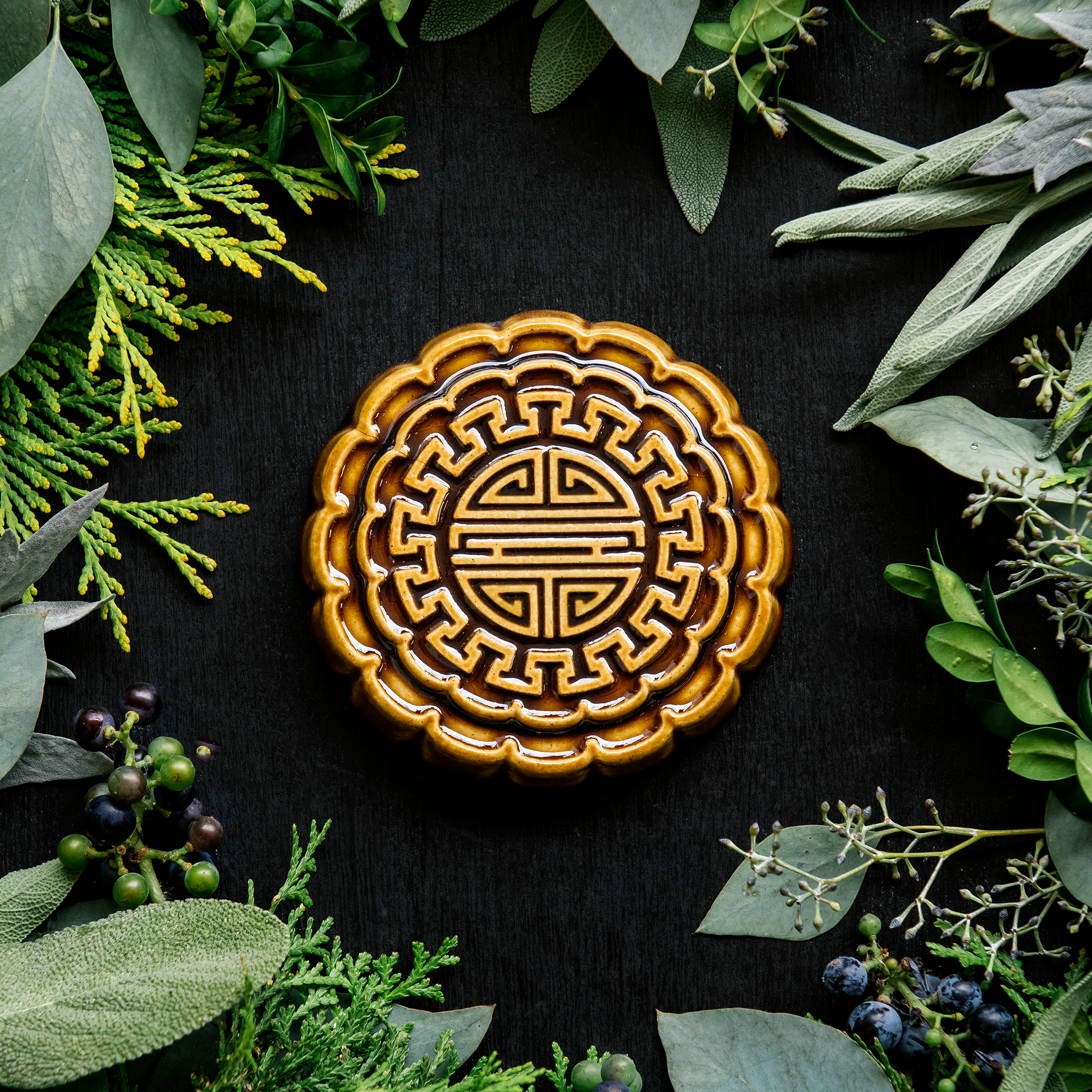 A Mooncake Paperweight in our glossy Molasses glaze, surrounded by cool greenery and delicate concord grapes.