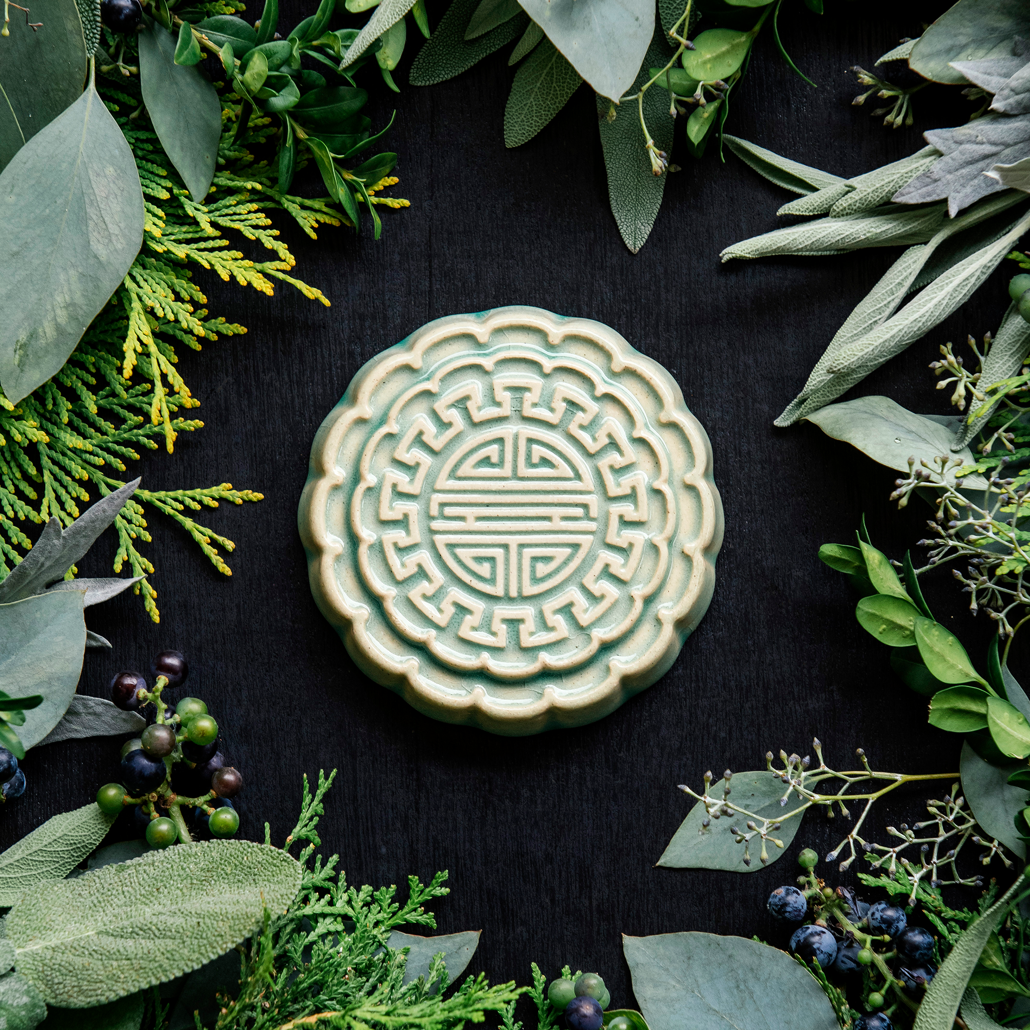 A Mooncake Paperweight in our glossy Celadon glaze, surrounded by cool greenery and delicate concord grapes. 