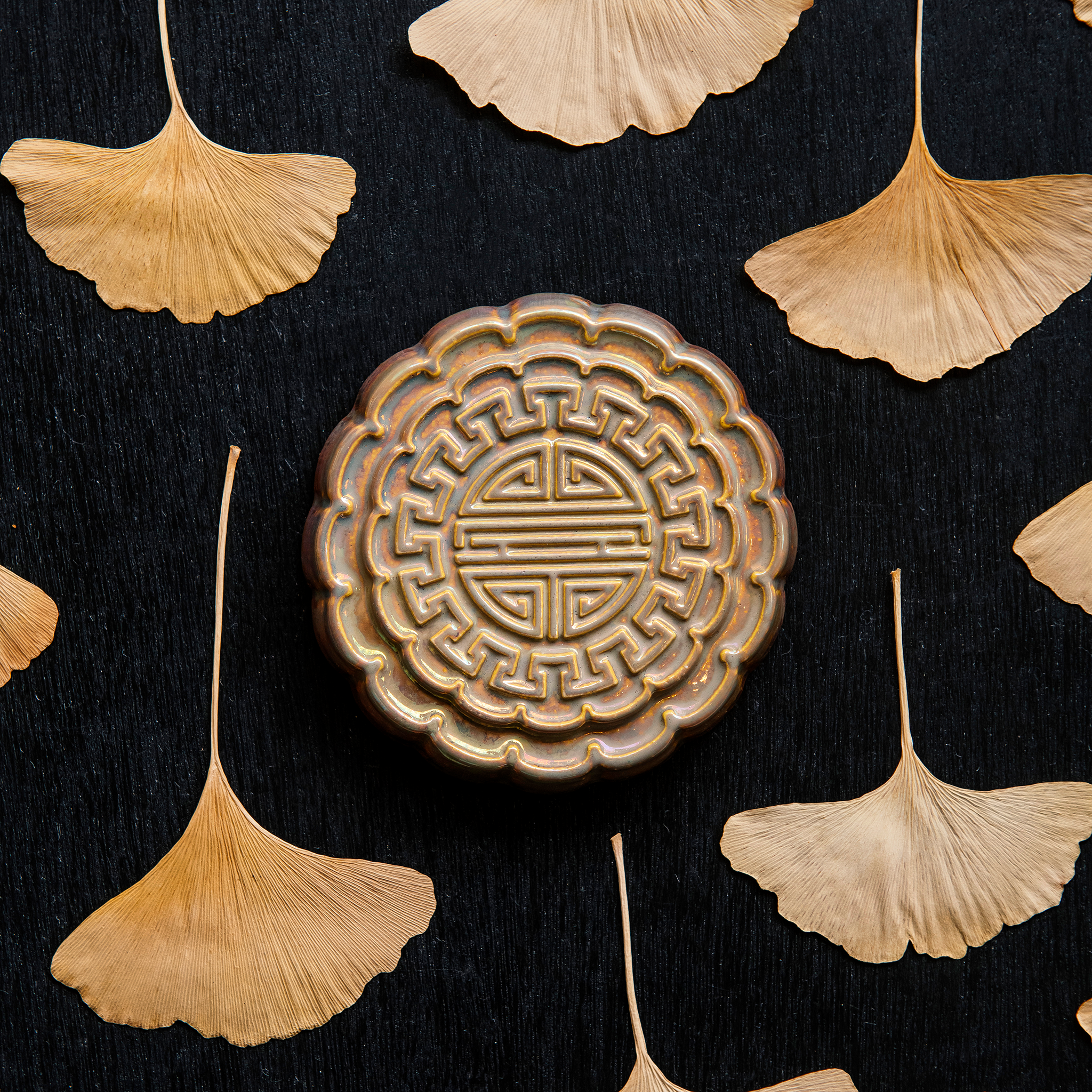 A Mooncake Paperweight in shimmering Blush Iridescent surrounded by dried ginkgo leaves. 