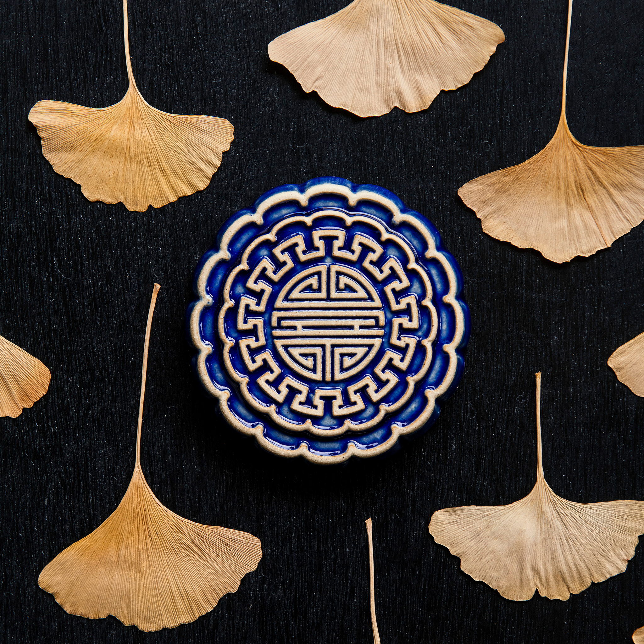 A Mooncake Paperweight in two-tone Lapis/Scrape surrounded by dried ginkgo leaves. 