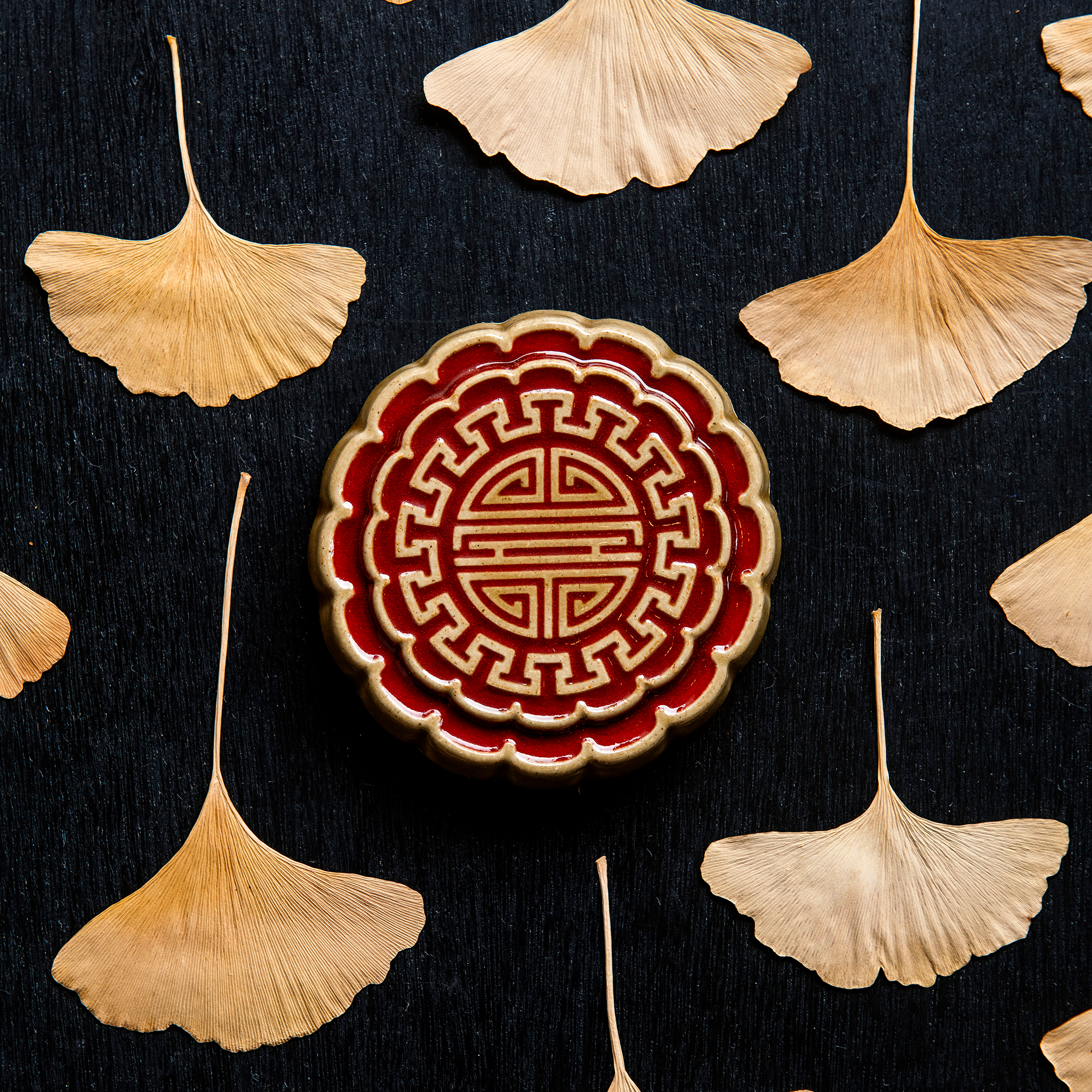 A Mooncake Paperweight in two-tone Scarlet/Honey surrounded by dried ginkgo leaves. 