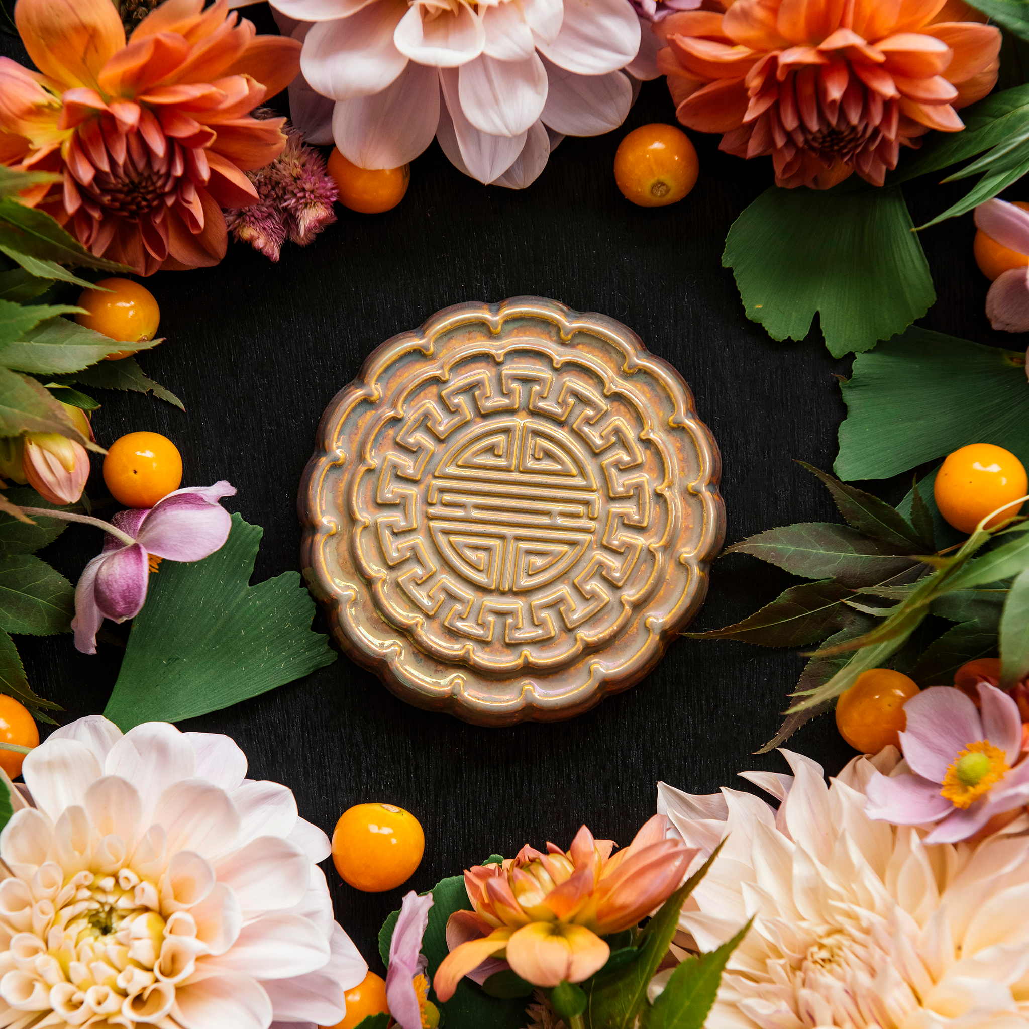 A Mooncake Paperweight in shimmering Blush Iridescent surrounded by vibrant summer florals and gooseberries. 