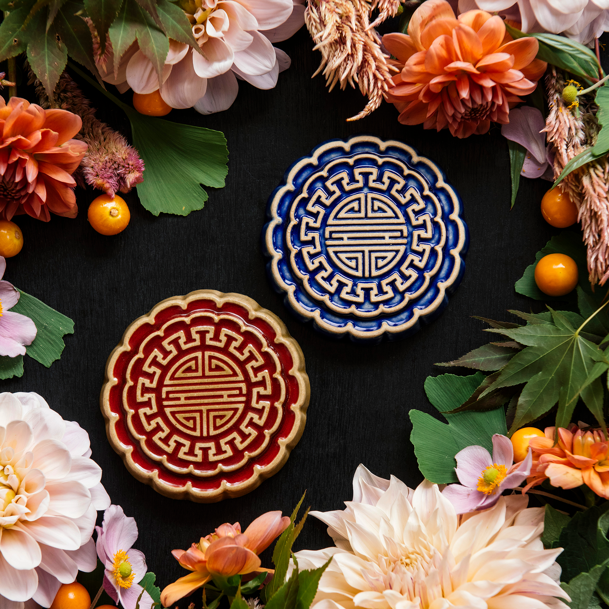 Two Mooncake Paperweights in two-tone Lapis/Scrape and Scarlet/Honey surrounded by vibrant summer flowers and gooseberries. 