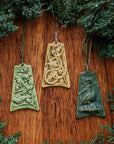 Three colorfully embossed ornaments are lay on a wood background with holiday greenery surrounding them: one has four parrots resting tree branches covered with berries, another has five intertwined rings with holly and berries strewn around them, the last has a goose keeping watch over her nest filled with six eggs.