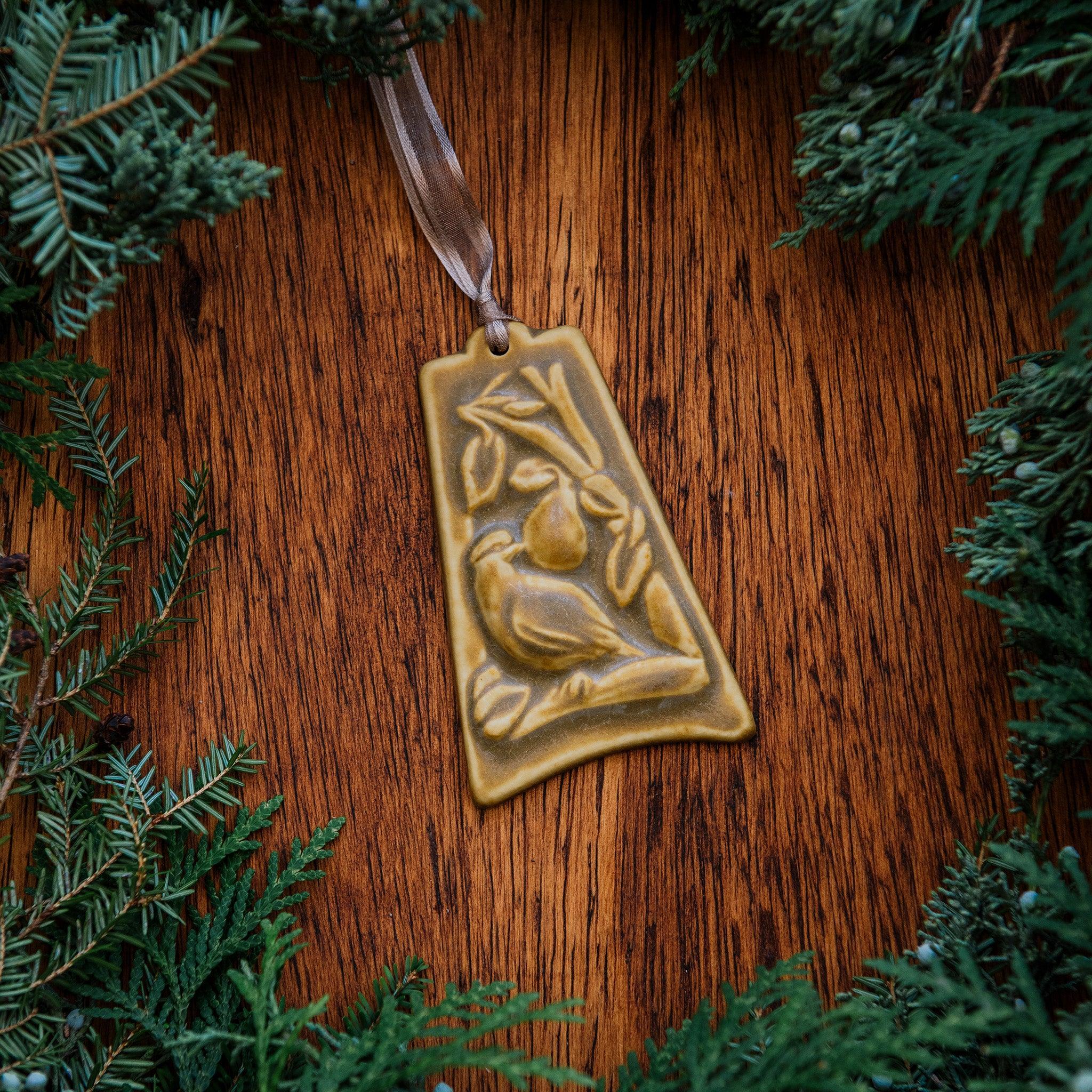 The bell-shaped Partridge in a Pear Tree Ornament features a partridge sitting on the branches of a tree with one large pear dangling from its branches. The ornament is glazed in a creamy brown color.