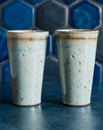 Two ceramic Pewabic Pints in a glossy Frost glaze against a blue hex tile background. 