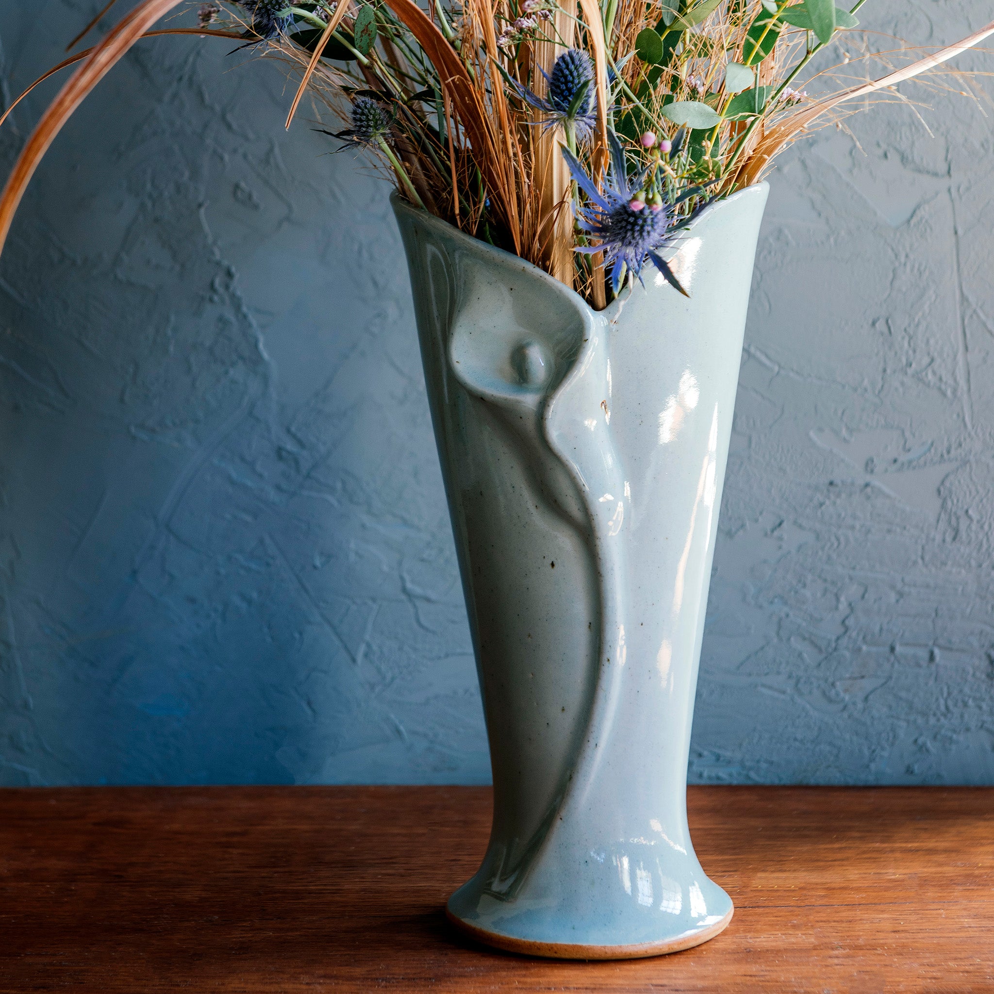 The calla lily vase fits a medium to large bouquet. The sides of the sleek vase start small at the base and slope out to create a large opening at the top. A high relief shape of a calla lily flower is front and center creating a modern, elegant look.