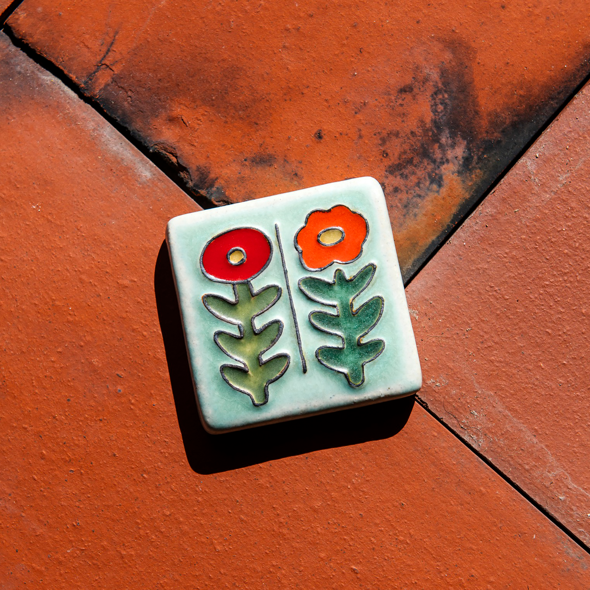 The Two Flowers Tile features two flowers on long, straight, leafy stems. One flower has scalloped petals while the other is circular.
