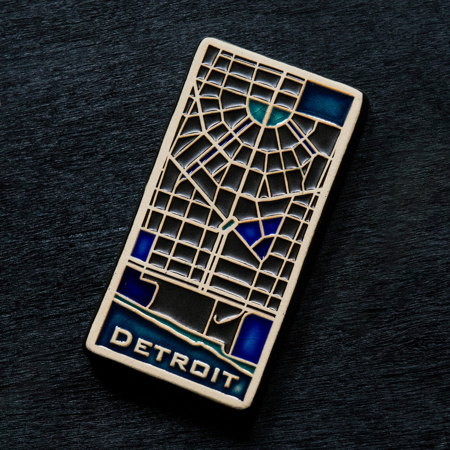 This hand painted tile is black with blue accents differentiating the water of the Detroit River and other specific areas of downtown including Campus Martius.