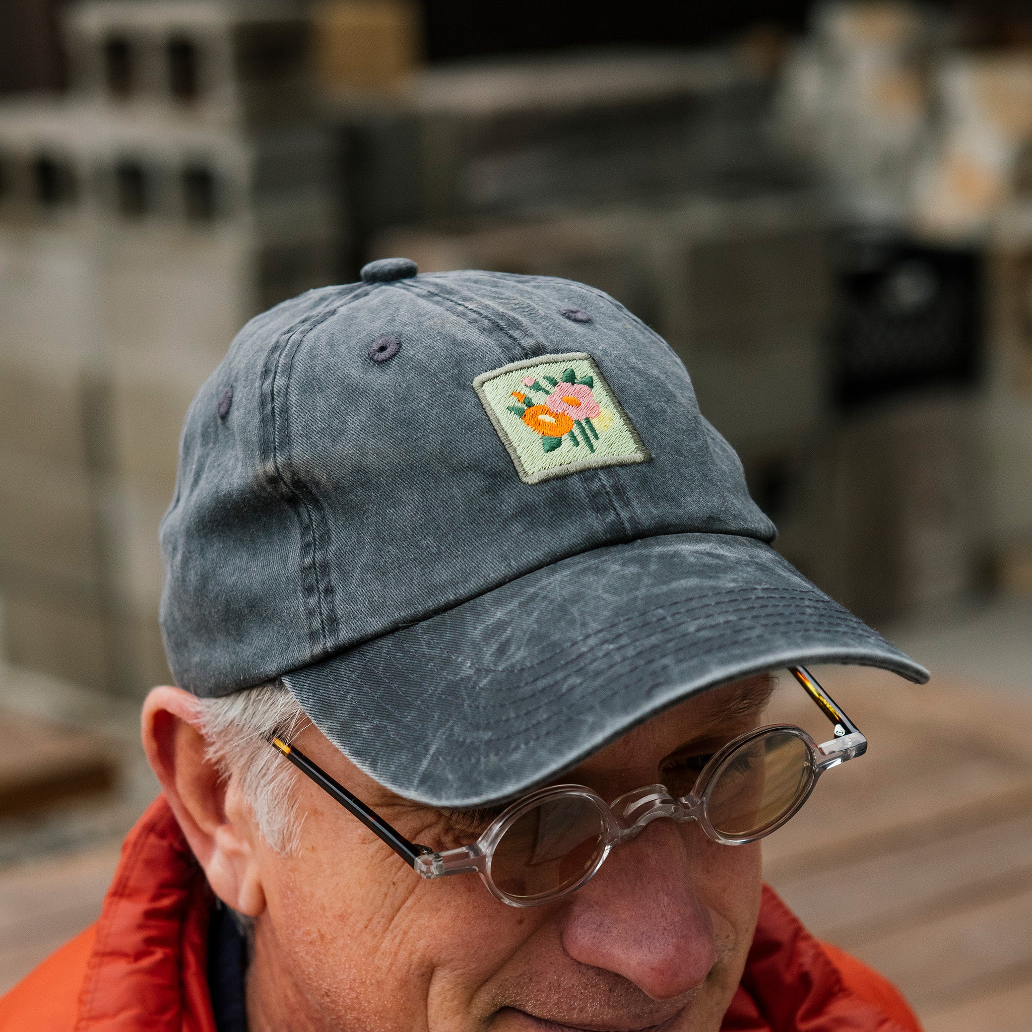 Man wearing a dark gray cap with a floral patch and sunglasses, outdoors.