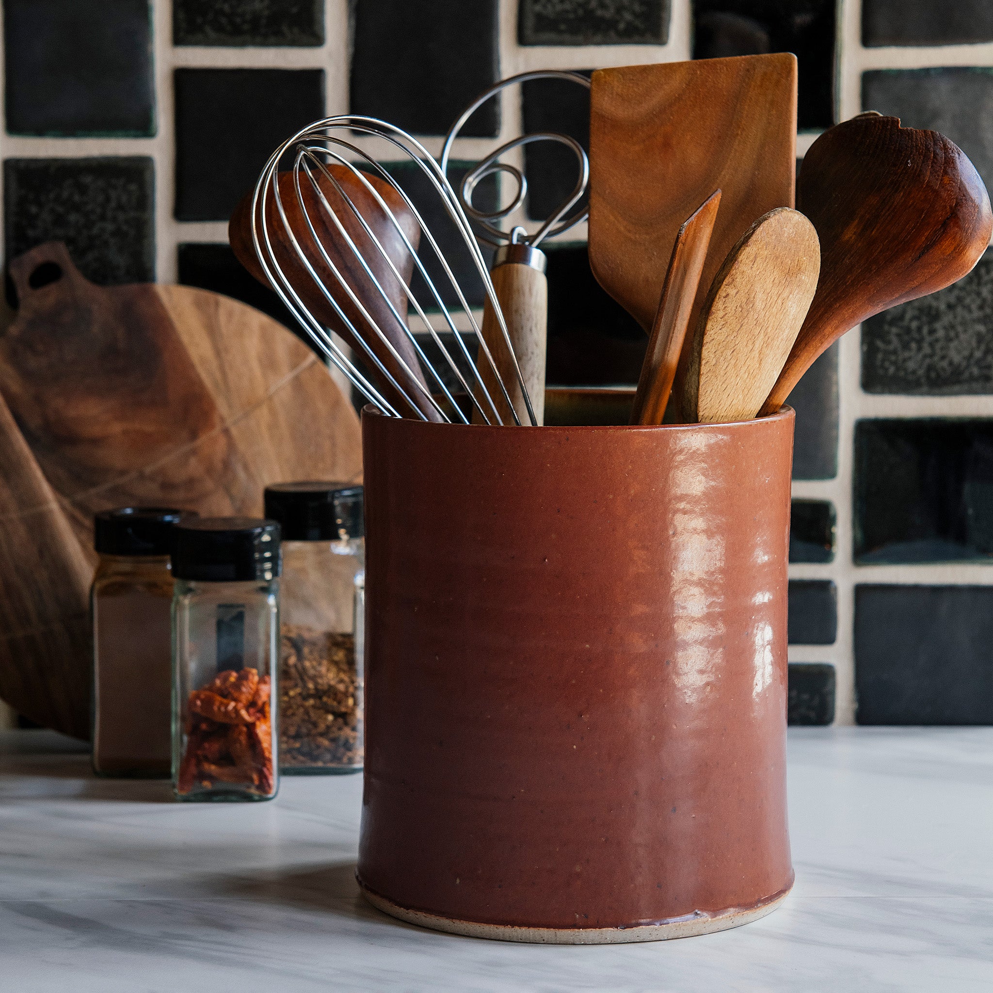 This Cinnamon glazed Crock sits in a modern black and white kitchen, holding wooden and metal cooking utensils.