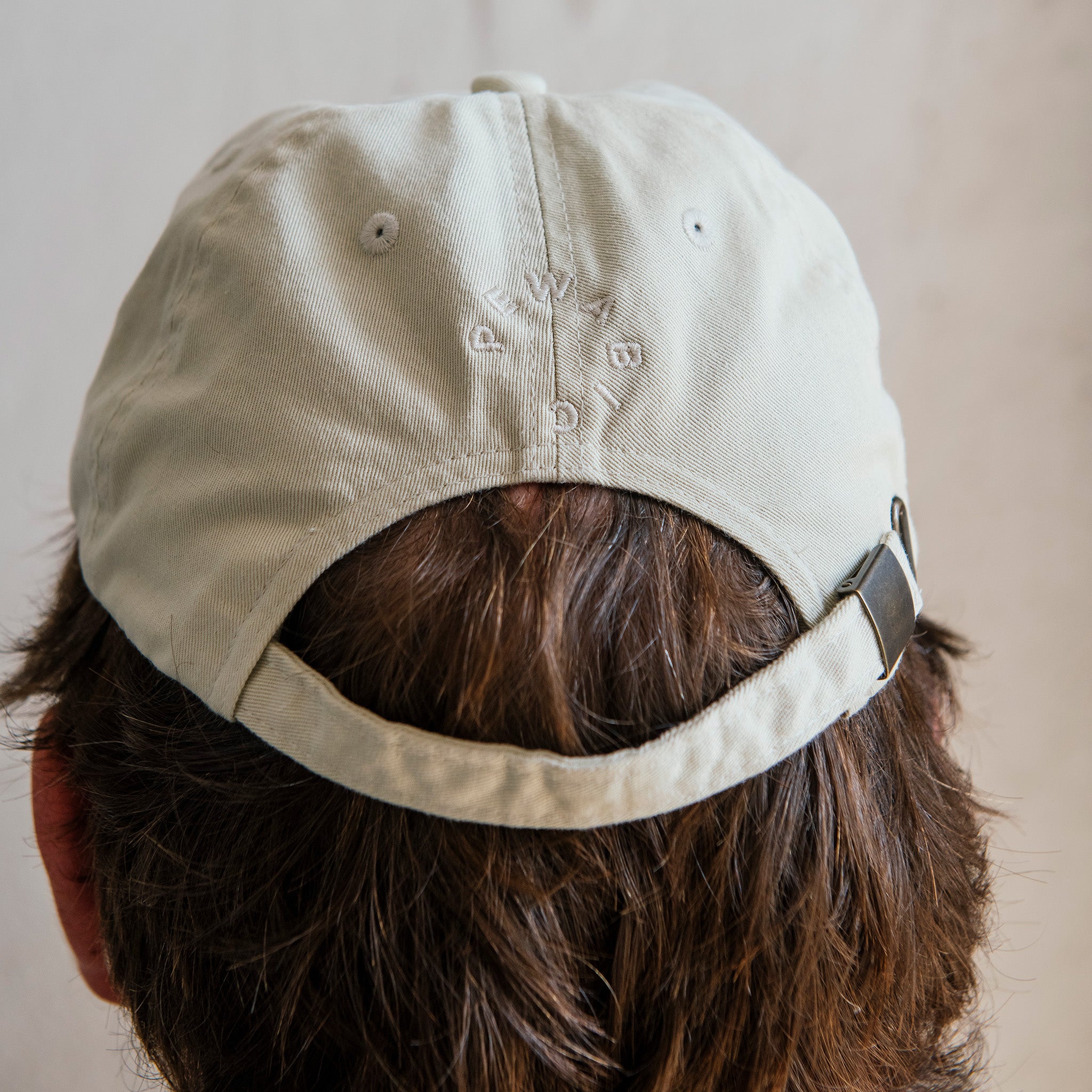 The back of the off-white hat features the Pewabic logo and adjustable fabric strap.