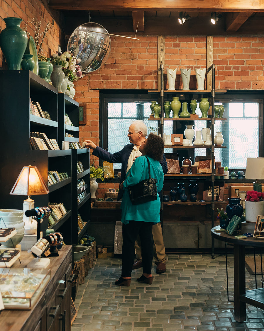 An older man and woman peruse a shelf full of tiles in the historic Pewabic gallery store.